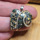 Jasper heart pendant held between fingers on a wooden surface