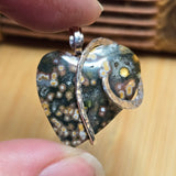 Heart-shaped pendant with speckled design held between fingers on a wooden surface
