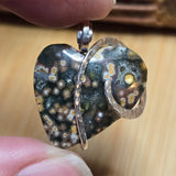 Close-up of a unique pendant with a textured surface held between fingers on a wooden background
