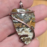 Hand holding a stone pendant with copper wire wrapping