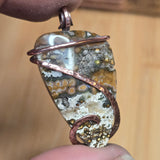 Pendant with natural stone and copper wire wrapping on a blurred background