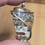 Close-up of a stone pendant with copper wire wrapping held between fingers against a blurred background