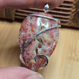 Pendant with red and white pattern held by a hand on a wooden surface