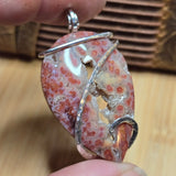 Close-up of a unique stone pendant with a silver wire wrap on a wooden surface.