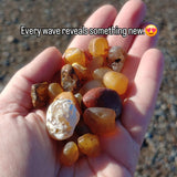 Hand holding multicolored stones with a beach background and text overlay.