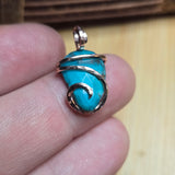 Turquoise stone pendant with gold wire wrapping on a finger against a wooden background