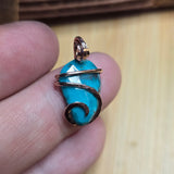Turquoise stone pendant with gold wire wrapping held between fingers on a wooden surface