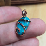 Turquoise stone pendant with rose gold wire wrapping held between fingers