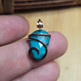 Turquoise stone pendant with rose gold filled wire wrap on a finger against a wooden background