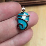 Turquoise stone pendant with gold wire wrapping on a finger against a blurred background