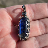 Blue stone pendant with silver setting held in a hand