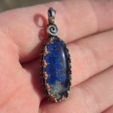 Pendant with blue stone and silver spiral design held in a hand