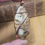 Hand holding a stone pendant with wire wrapping against a wooden background