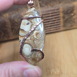 Hand holding a stone with copper wire wrapping against a wooden background