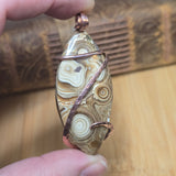 Hand holding a stone pendant with copper wire wrapping against a wooden background