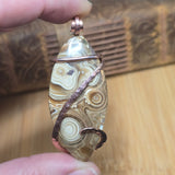 Hand holding a stone pendant with wire wrapping against a wooden background