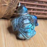 Turtle-shaped stone pendant with metallic sheen on a wooden surface