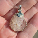 Crystal pendant with silver spiral design held in a hand