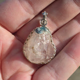Close-up of a hand holding a crystal pendant with a silver setting.