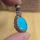 Turquoise pendant with silver and copper accents held between fingers against a blurred background