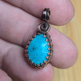 Turquoise pendant with copper wire wrapping held between fingers on a wooden surface