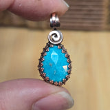Turquoise pendant with copper accents held between fingers against a blurred background