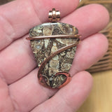 Hand holding a stone pendant with a copper wire wrap