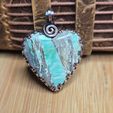 Green variscite heart-shaped pendant with a silver spiral on a wooden background