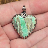 Heart-shaped variscite pendant with copper accents held in a hand.