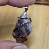 Hand holding a stone pendant with copper wire wrapping on a wooden surface