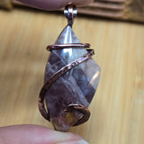 Close-up of a stone pendant with copper wire wrapping held by a hand on a wooden surface.