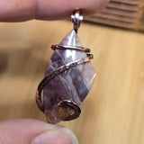 Hand holding a stone pendant with copper wire wrapping against a wooden background