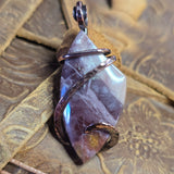 Purple stone pendant with copper wire wrapping on a textured brown background