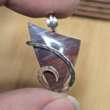 Close-up of a unique silver and stone pendant held between fingers against a blurred background