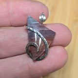 Silver pendant held between fingers with a wooden background
