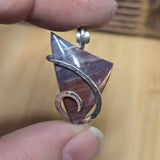 Hand holding a purple stone pendant with silver wire wrapping against a wooden background