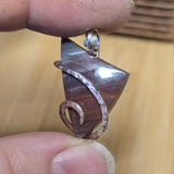 Hand holding a silver and purple pendant against a blurred background