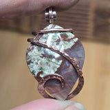 Close-up of a stone pendant with copper wire wrapping held between fingers.