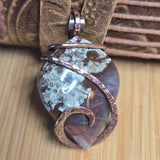 Copper-wrapped stone pendant on a wooden surface