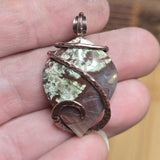 Copper-wrapped pendant with a natural stone design held between fingers.