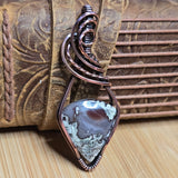 Copper wire-wrapped pendant with a natural stone on a wooden surface