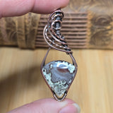 Jewelry with a stone and wirework held by a hand against a wooden background