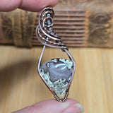 Hand holding a decorative pendant with a textured stone center on a wooden surface