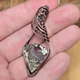 Copper wire-wrapped pendant with a natural stone on a hand