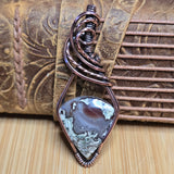 Copper wire-wrapped pendant with a stone on a textured leather surface