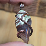 Hand holding a pendant with a natural stone and copper wire wrap against a blurred background