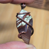 Hand holding a copper-wrapped stone pendant against a blurred background