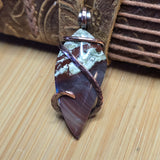 Jewelry pendant with stone and copper wire wrapping on a textured surface