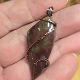 Hand holding a leaf-shaped pendant with copper wire wrapping