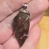Brown stone pendant with silver setting held in a hand against a blurred background